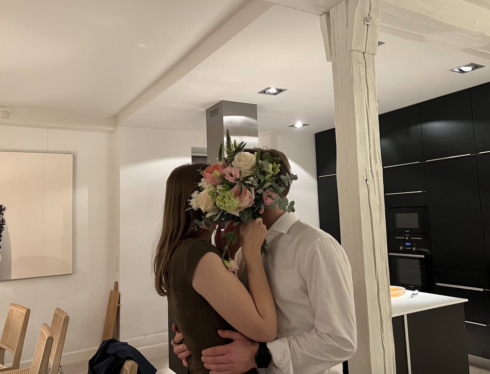 Leonard and Mona kissing behind a wedding bouquet Mona caught in Denmark