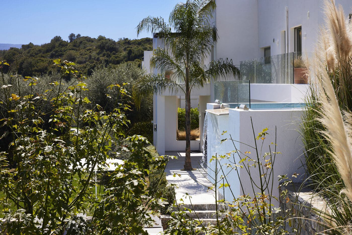 Infinity pool with waterfall feature surrounded by olive and palm trees